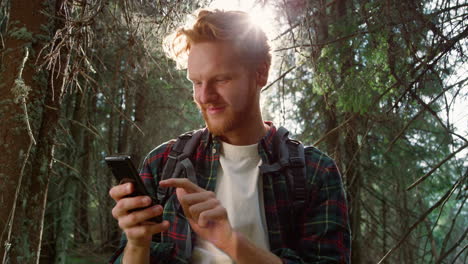 traveler using smartphone in woods. redhead man texting message on cellphone