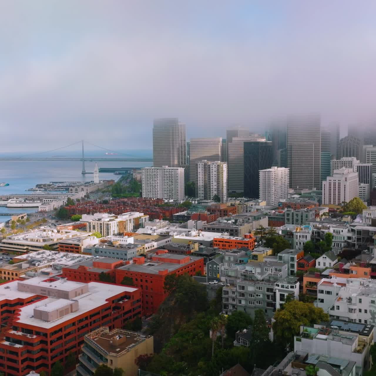 Flying over the gorgeous houses at the bay. Approaching the docks and blue waters of Pacific. San Francisco skyscrapers in the fog