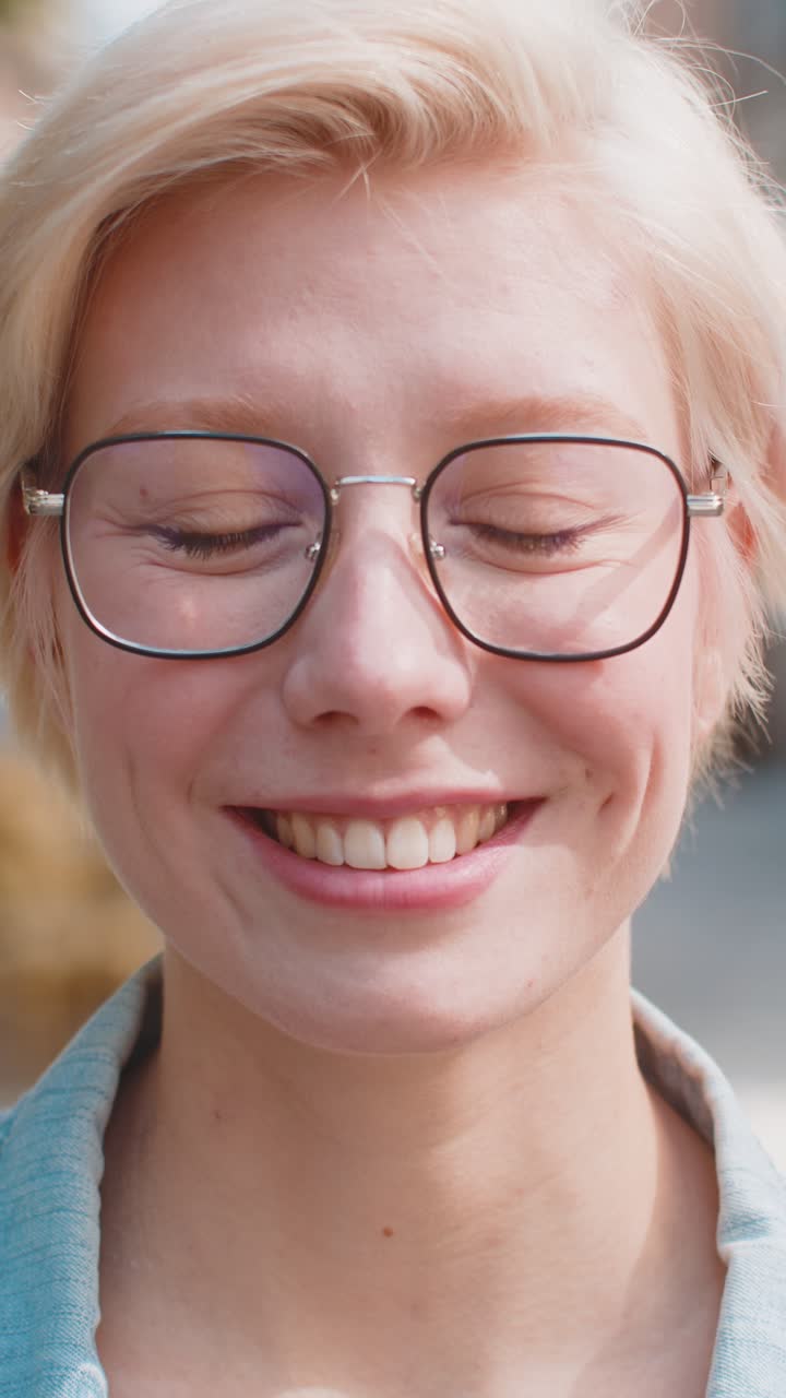 Portrait of happy caucasian young woman in glasses smiling while looking at camera on city street