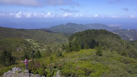 A-man-standing-on-a-high-view-point-of-the-Madeira-mountains-in-Portugal-and-raising-his-arms-to-mother-nature---Aerial-shot