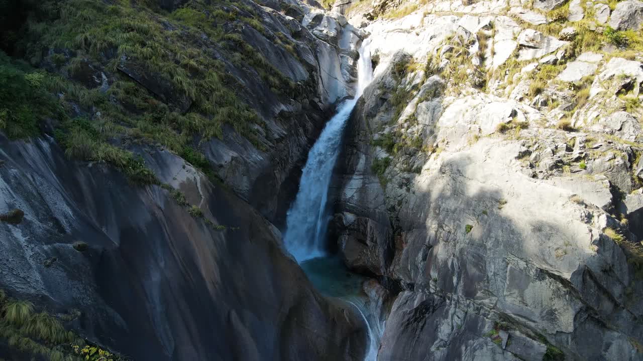 una toma aérea de un dron que muestra una hipnotizante cascada que fluye a través del accidentado terreno montañoso.
