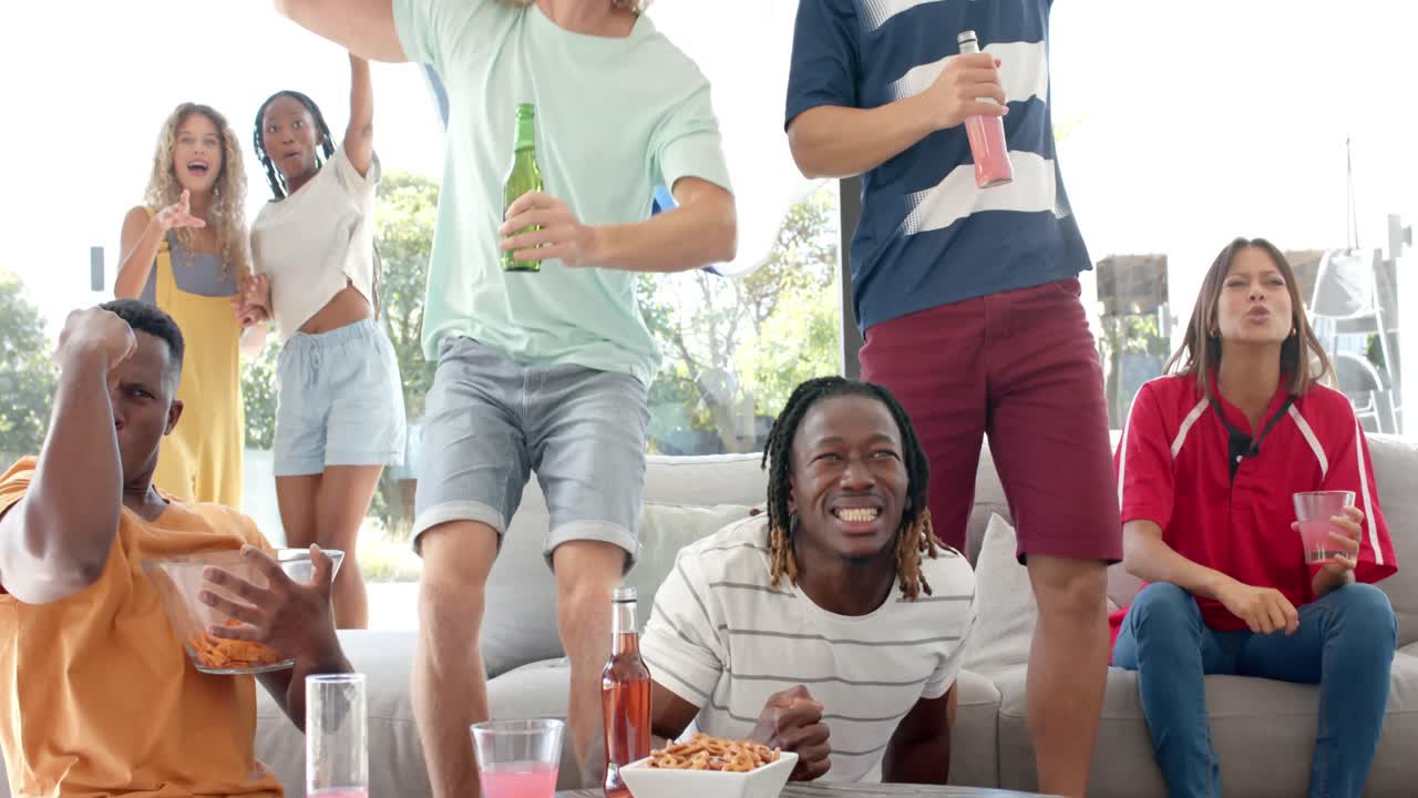 amigos diversos emocionados con bebidas y banderas viendo deportes en la televisión y celebrando, cámara lenta