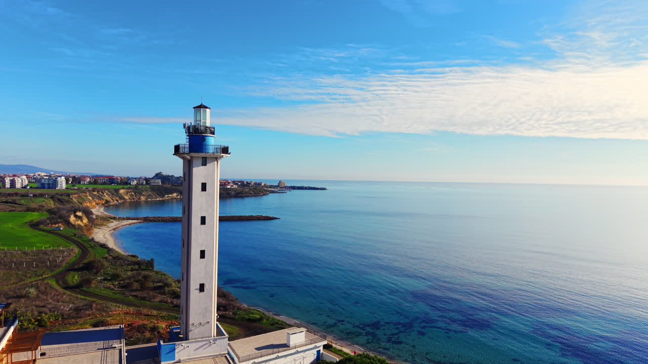 Vista aerea di un alto faro bianco con la cima blu, edifici residenziali con tetti rossi, campi verdi e un mare blu calmo sotto un cielo sereno. Bulgaria