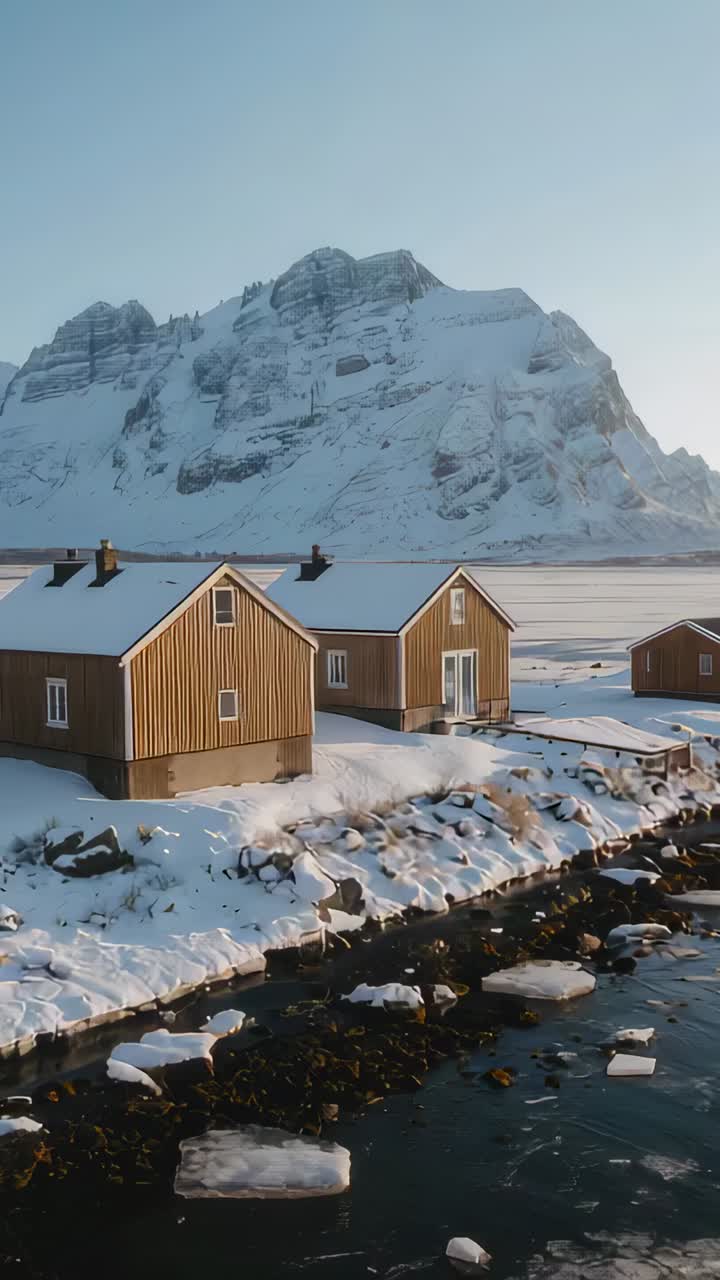 Vertikal video: Panorerende kamera som avslører tre hytter på snødekt strandlinje med glassdør og brygge