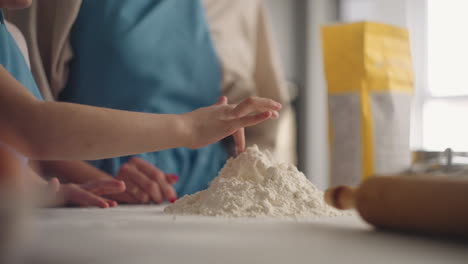 woman is showing to her little daughter how to make dough for pie or cake cooking together in home kitchen