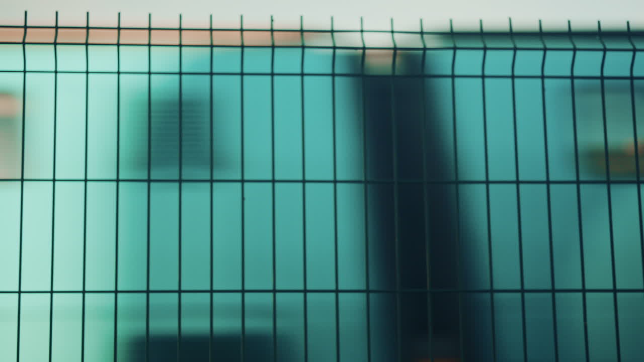 Blurred train passing behind a metal fence, creating an abstract transportation scene with strong graphic lines