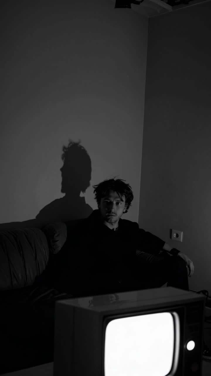 hombre sentado en una habitación oscura viendo televisión vintage