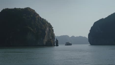 lan ha bay with boat sailing in between towering limestone cliffs in vietnam in background