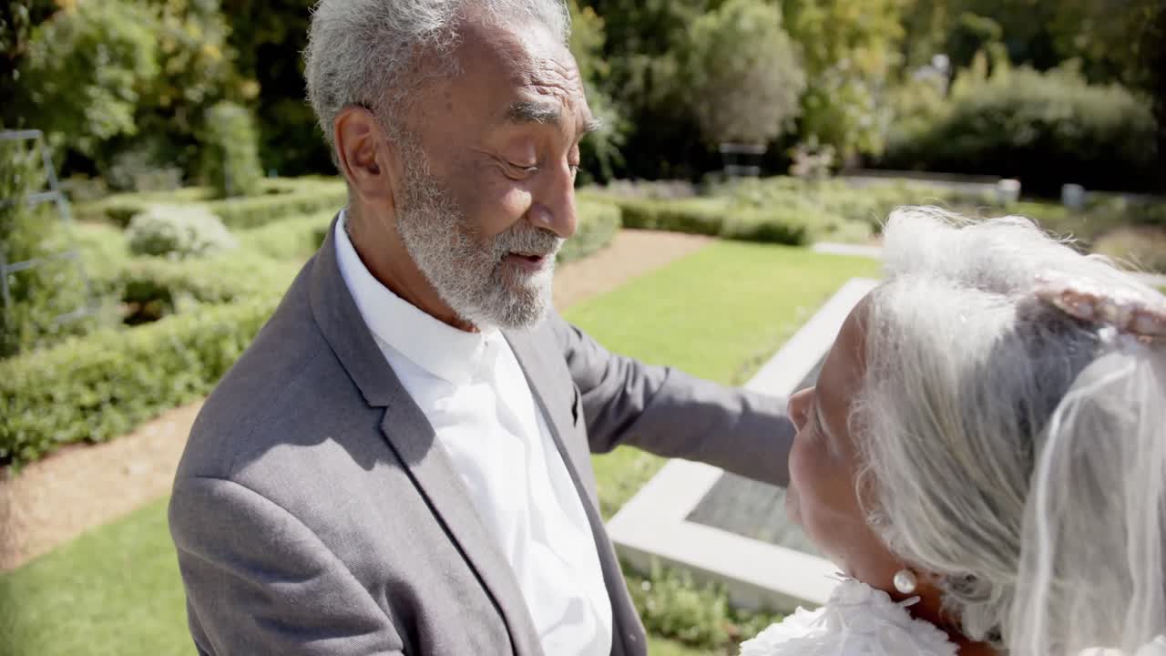 feliz pareja biracial senior caminando, bailando en la boda en el jardín, cámara lenta