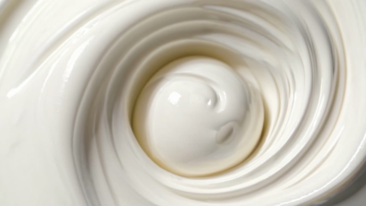 Close-up, top-down view of smooth, swirling cream texture, resembling a video of a gentle, hypnotic