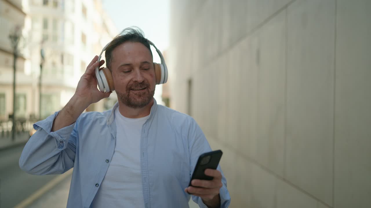 joven caucásico sonriendo confiado escuchando música en la calle