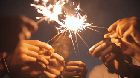 camera focuses on the hands of a group of friends who light flares at dusk