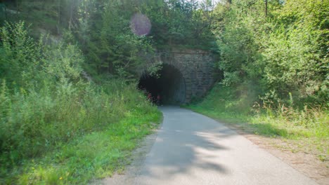 family cycling on bikes on strekna cycle path out of tunnel in slovenia. slow motion, follow shot