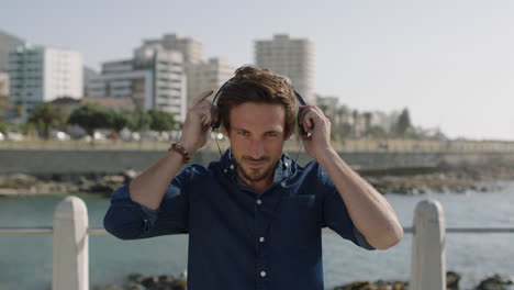 portrait-of-attractive-young-caucasian-man-puts-on-headphones-listening-to-music-on-beachfront