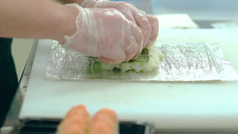 el cocinero prepara sushi japonés con camarones, arroz y algas nori. pone las gambas.