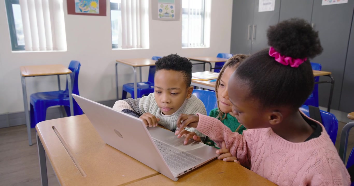 Bambini afroamericani che si sporgono verso un laptop argentato, premendo i tasti a turno per il lavoro in classe