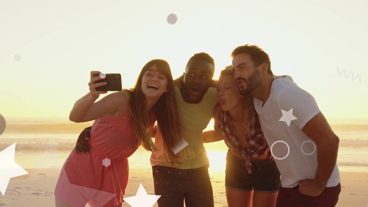Donna che alza il cellulare in un gruppo, sporgendosi su una spiaggia al tramonto, con sovrapposizioni che oscurano la visualizzazione della foto per i social media.