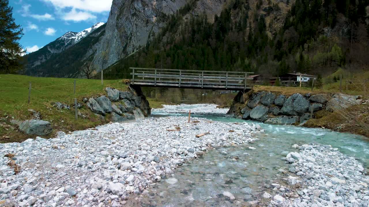 un dron aéreo bajo y cercano vuela a través del vuelo debajo de un puente en el pintoresco valle de ahornboden engtal a lo largo del río de montaña rissach en los alpes austriacos bávaros en un día nublado y soleado en la naturaleza