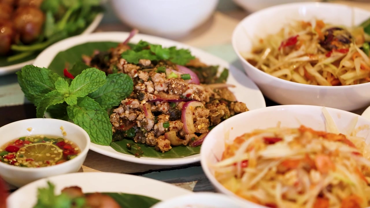 Rekaman panning jarak dekat hidangan khas Thailand termasuk salad pepaya dan daging babi cincang pedas
