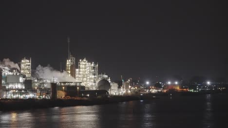 Riverside-Beleuchtete-Industriefabrik-Mit-Schornsteinrauch-In-Der-Nacht