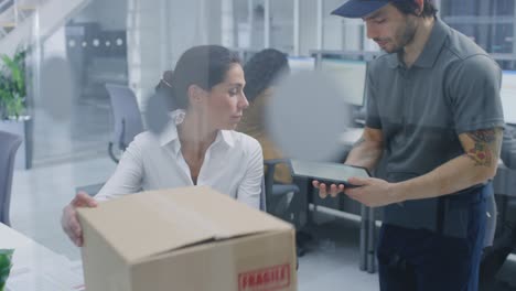 in corporate office beautiful businesswoman working on desktop computer delivery man enters and hands her postal package, she signs tablet computer and thanks him. modern office
