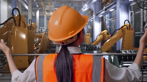 close up back view of a female engineer with safety helmet spreading arms while standing with industrial robotic arms working