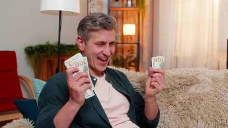 young man smiles while counting cash dollars in hands expresses joy from income and financial gain