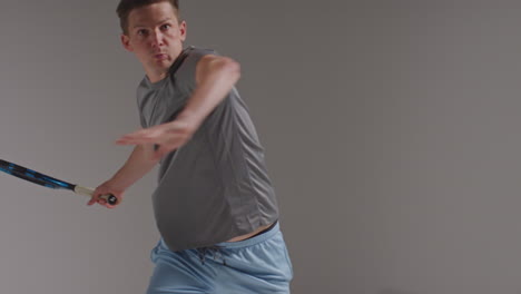 studio shot of male tennis player returning shot in match hitting ball with racket against grey background 3