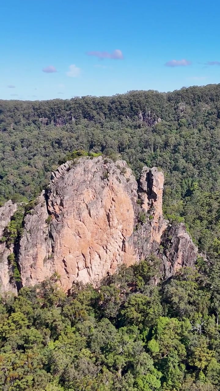 Riprese con drone catturano imponenti formazioni rocciose vulcaniche circondate da una fitta foresta verde sotto cieli azzurri.
