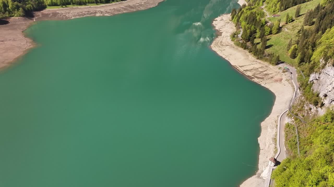 Aerial top-down view of the turquoise waters and rocky shoreline of Klöntalersee in Glarus, Switzerland, surrounded by dense green forest