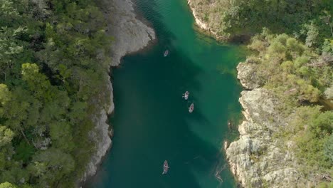 SLOWMO---People-on-kayak-trip-paddle-boats-through-canyon-on-Pelorus-river,-New-Zealand-with-native-forrest-and-rock-boulders---Aerial-Drone