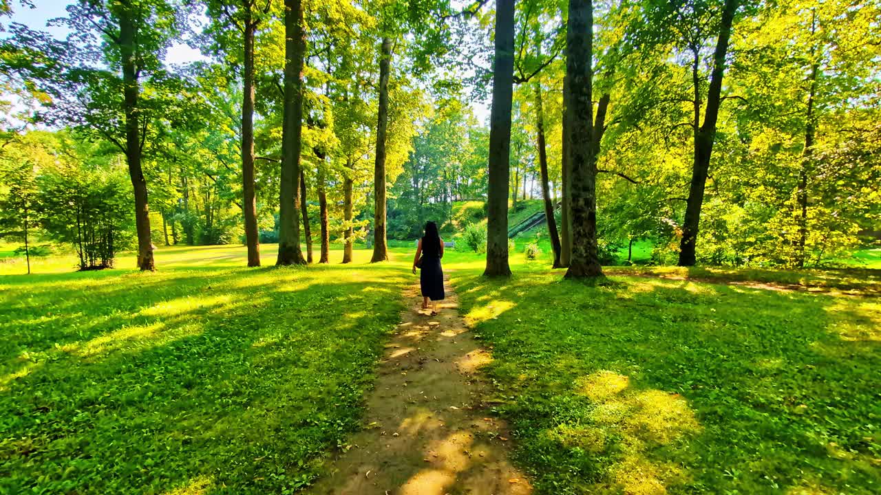 Woman walking in a sunlit forest path in Jaunpils, Latvia, peaceful mood