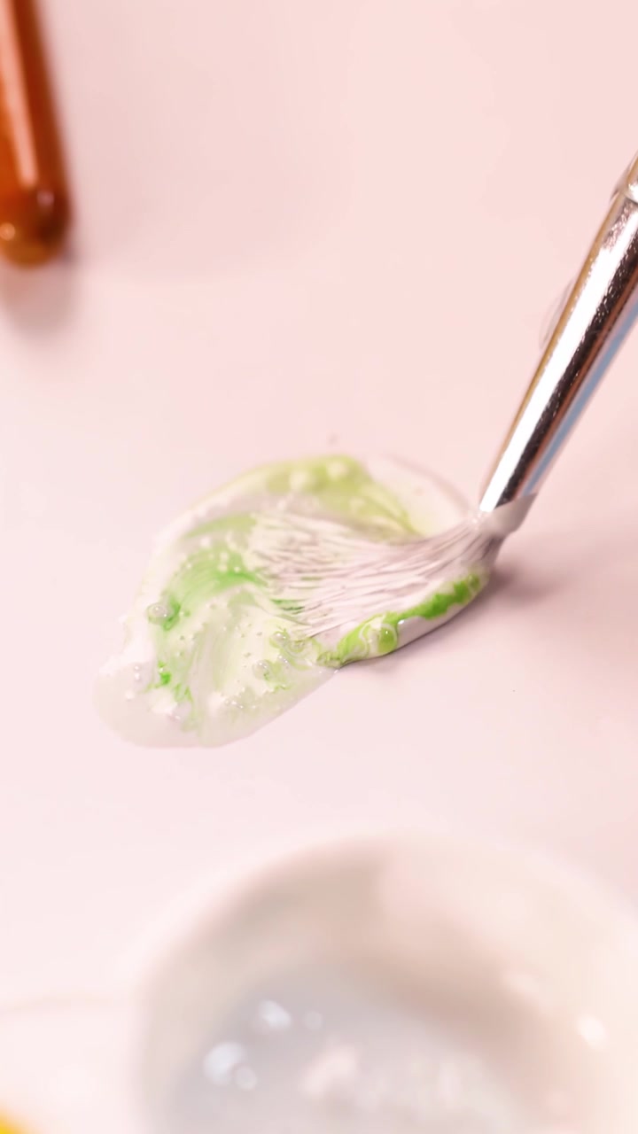 Un artista mescola pigmento verde nella pittura acrilica bianca usando un pennello sotto una luce soffusa da studio.