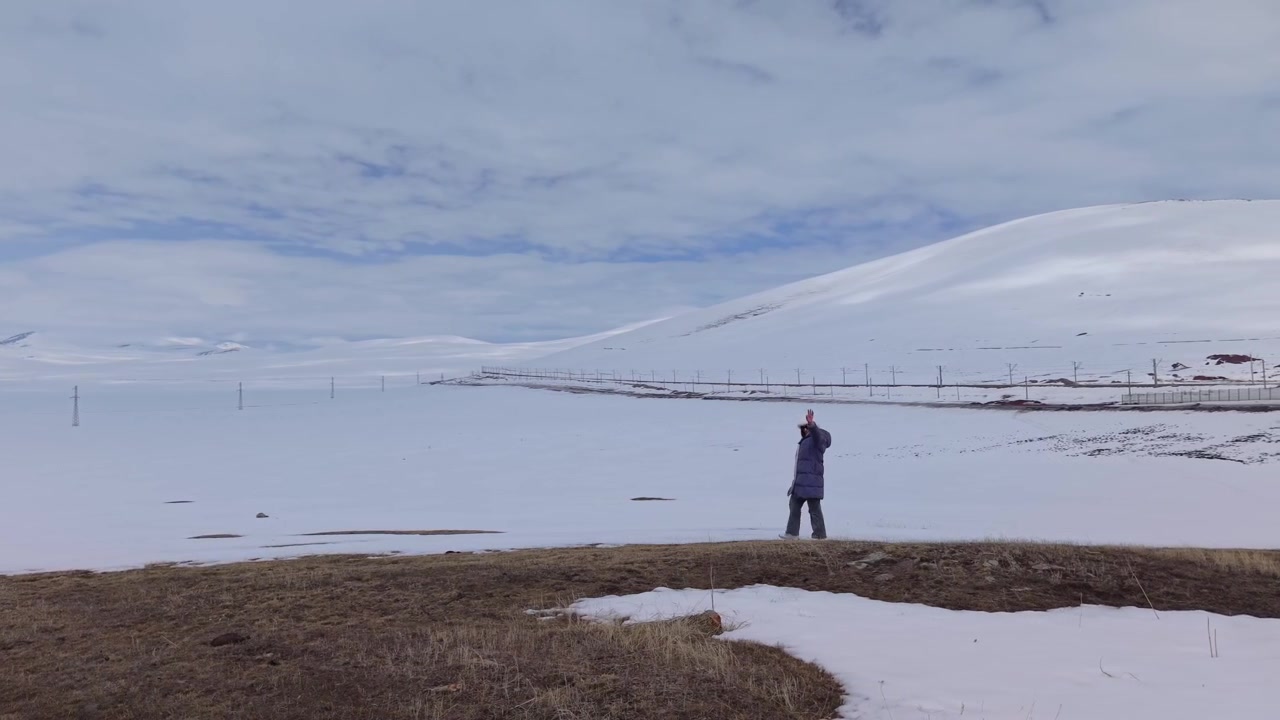 Footage of a woman walking through a minimal landscape with endless white ground and deep blue sky, creating a clean and surreal visual scene.