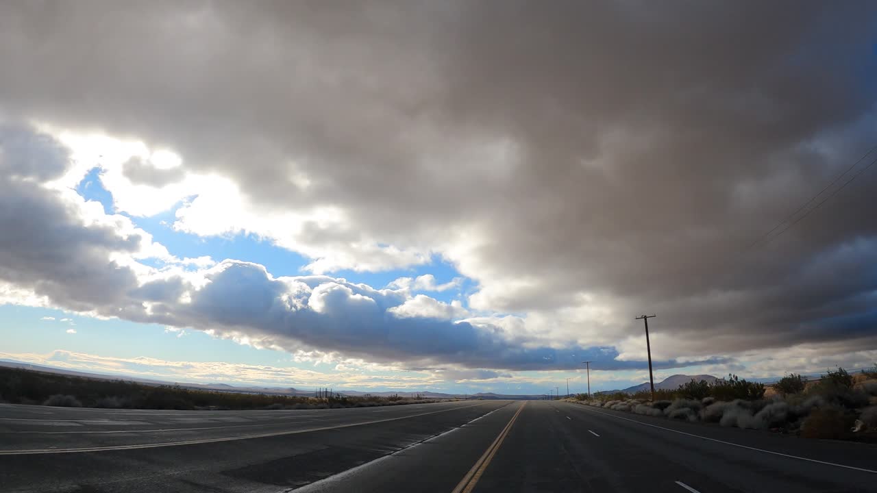 conduciendo a lo largo de una carretera casi vacía en el desierto de mojave con nubes ominosas y dramáticas sobre su cabeza - punto de vista