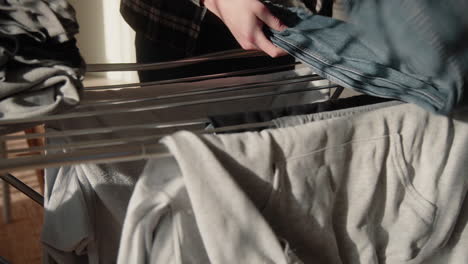 young male collecting and folding dry clean clothes from dryer at home in sunlit modern living room grey t-shirt and blue jeans close up 4k