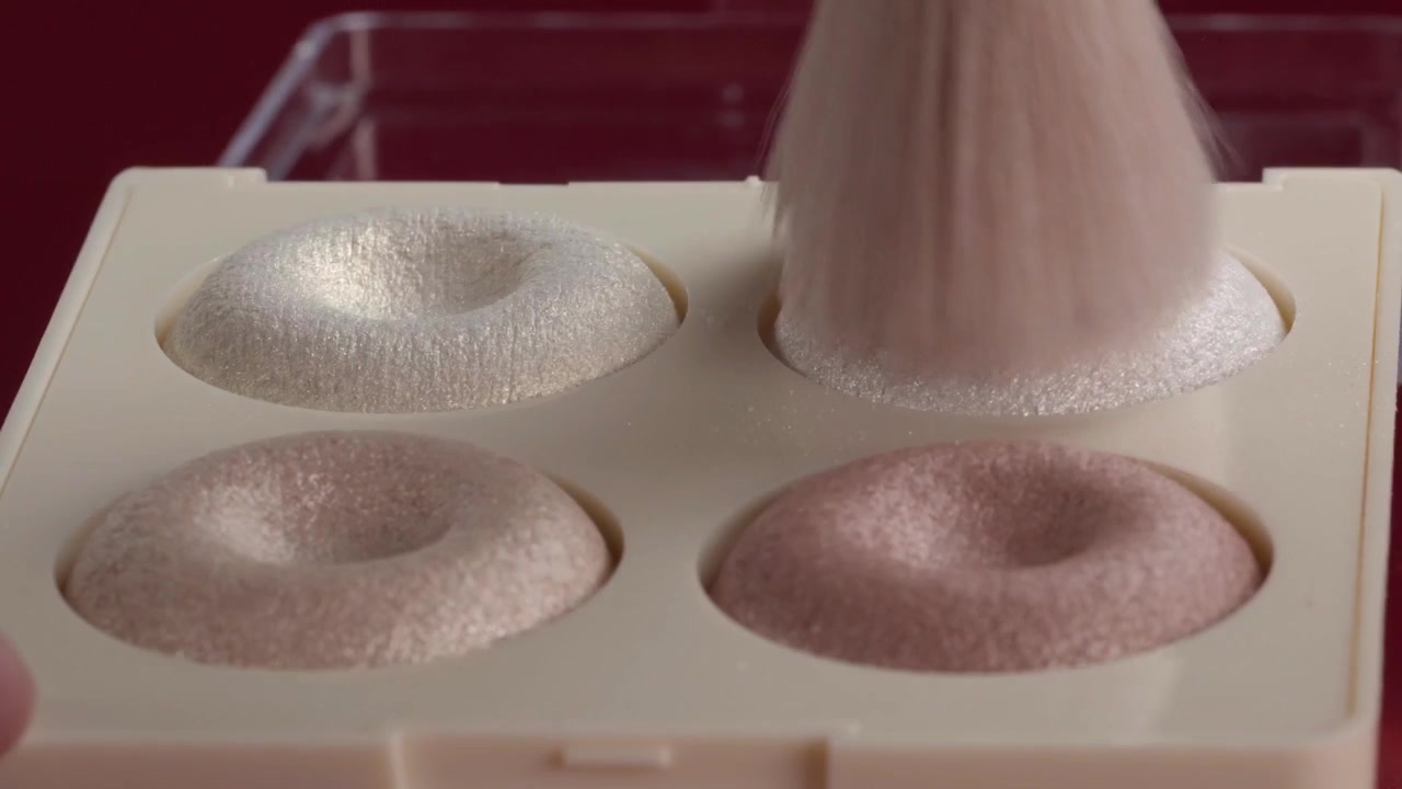 Close up of makeup brush being pressed into powder palette with soft pink, beige and white shades during cosmetic application