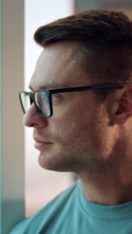 calm relaxed pensive man in glasses standing at the window with phone in hand. confident businessman takes off the glasses smiling to camera. vertical video