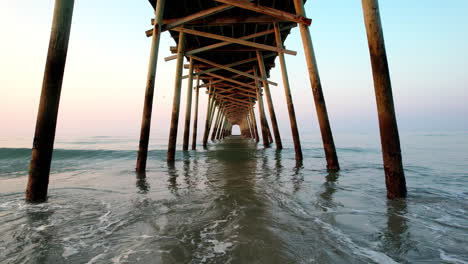 Drone-shot-slowly-moving-forward-underneath-a-pier-with-small-ocean-waves