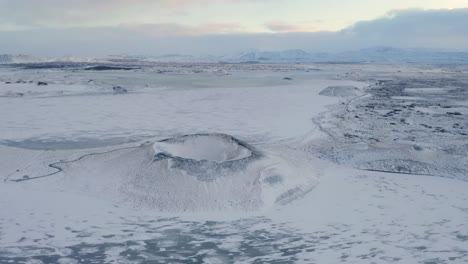 toma de órbita aérea del cráter volcánico nevado y el lago congelado my vatn en segundo plano durante el día de invierno en islandia