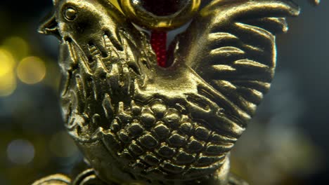 Estatua-Del-Zodíaco-Del-Pollo-Dorado-Tradicional-Del-Año-Nuevo-Chino,-Gallo-Dorado-Brillante-Colgado-Sentado-En-Monedas-De-Dinero-Símbolo-Asiático,-Fondo-Brillante-Con-Profundidad-De-Campo-Borrosa,-Macro-Panorámica-Izquierda-4k