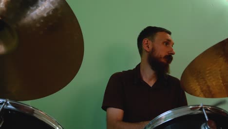 drummer warming up with drum brushes. bearded man playing rock and metal music on drums on green wall background. music band rehearsal jamming 4k footage.