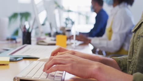 Mid-section-of-woman-typing-on-computer-keyboard-at-office