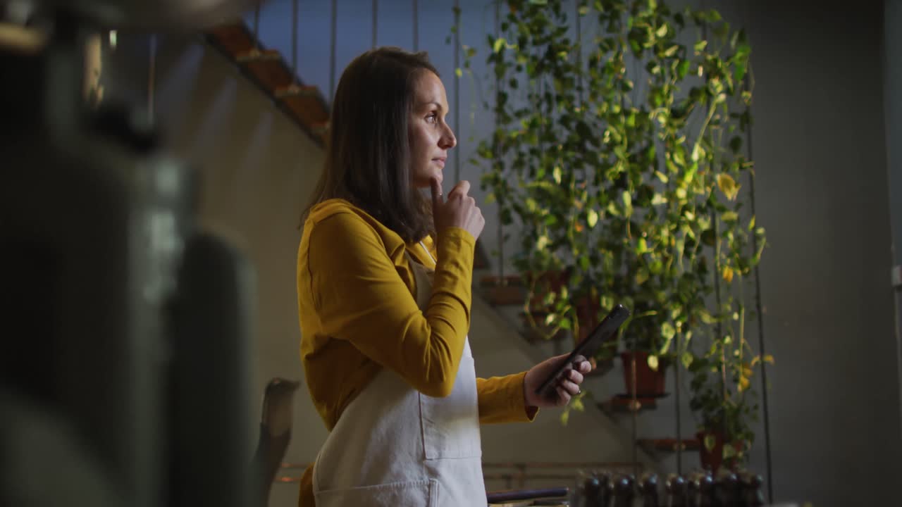 perfil de una joyera caucásica en un taller con un delantal, usando una tableta, sonriendo