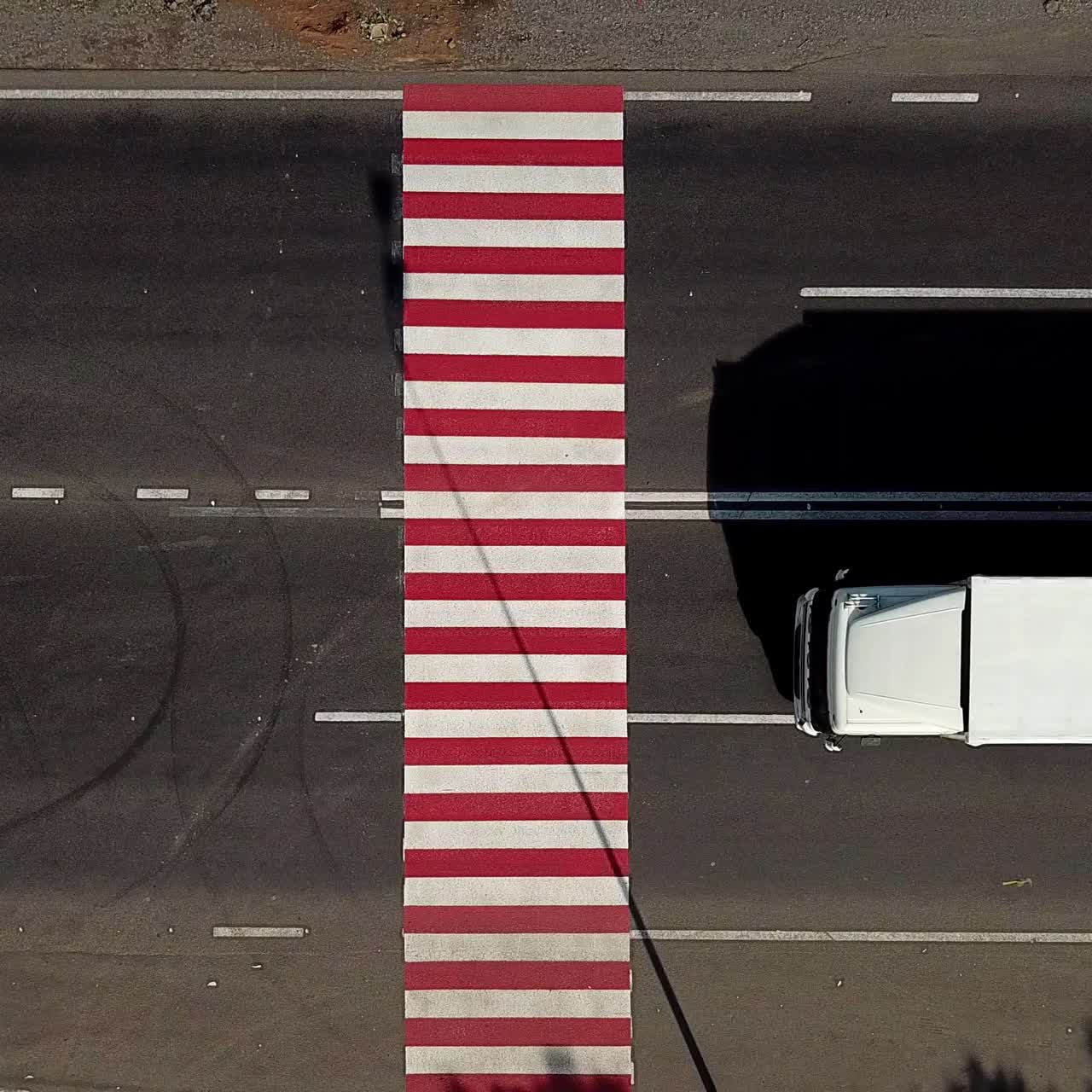 trucks are driving on the highway with a pedestrian crossing in red and white colours. Aerial view