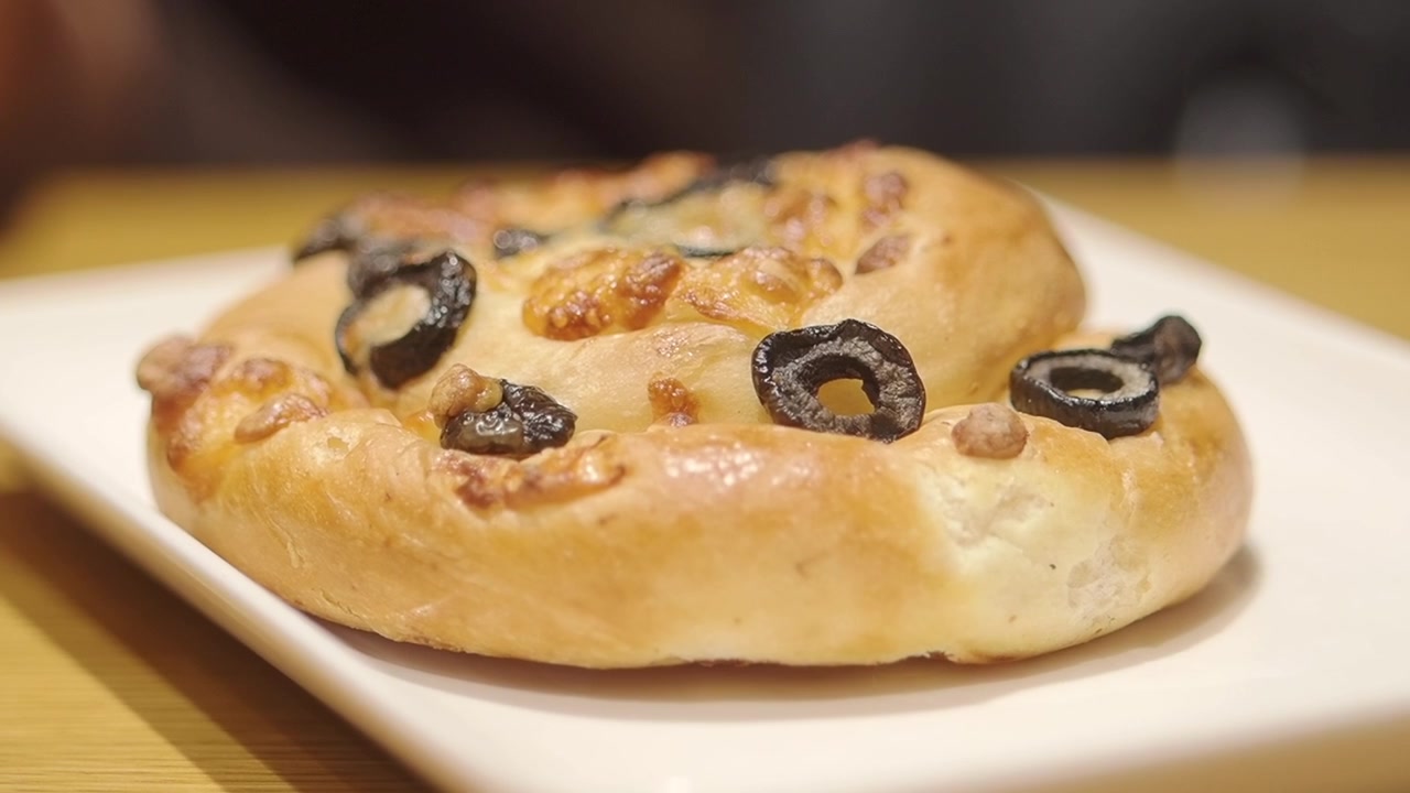 Mano che prende un panino alle olive appena sfornato dal piatto