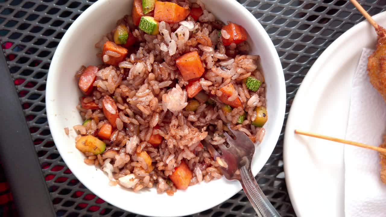 Colorful fried rice with vegetables and skewered snack on outdoor metal table