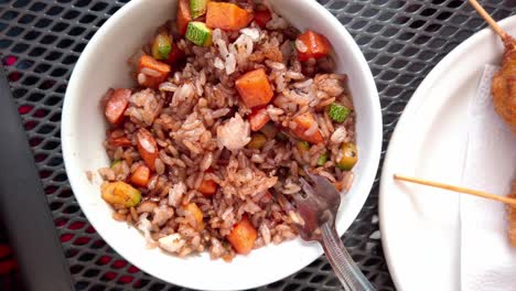 colorful fried rice with vegetables and skewered snack on outdoor metal table