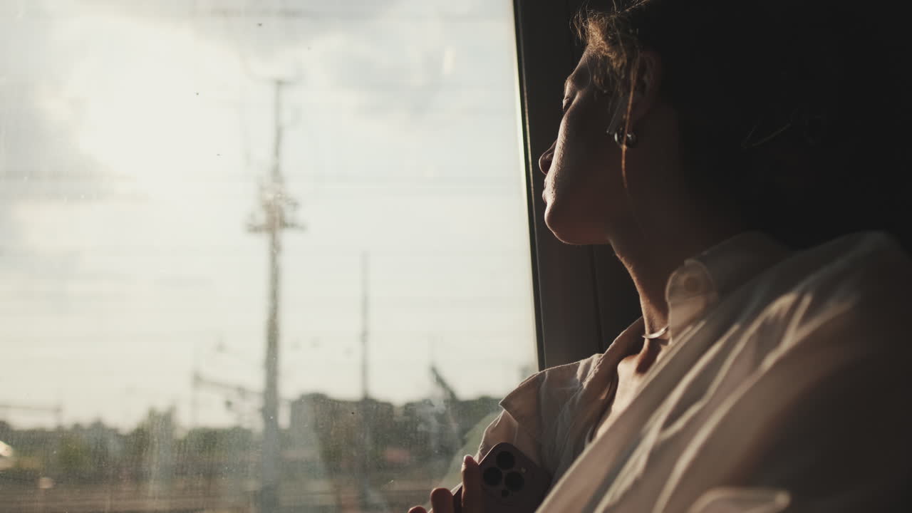 Thoughtful Woman Looks Out Train Window at Moving Urban Landscape