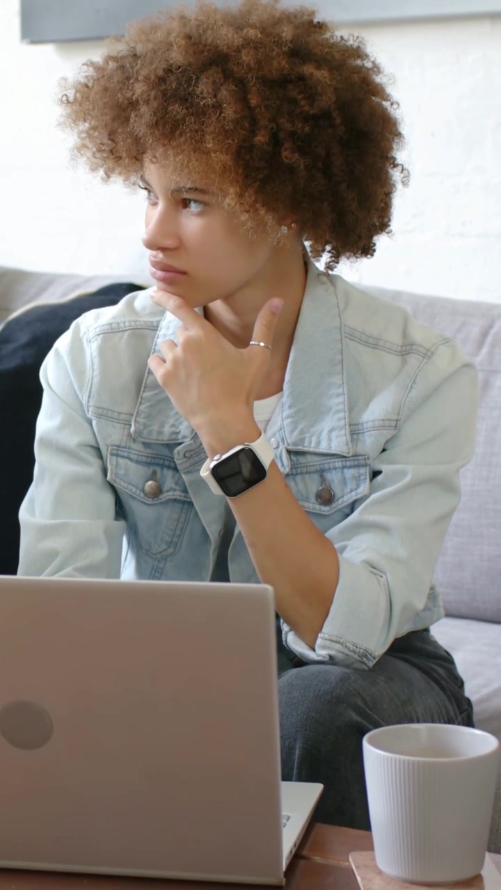 Video verticale: Donna con giacca di jeans che legge dal laptop, passando dal pensare al digitare a casa per rispondere.